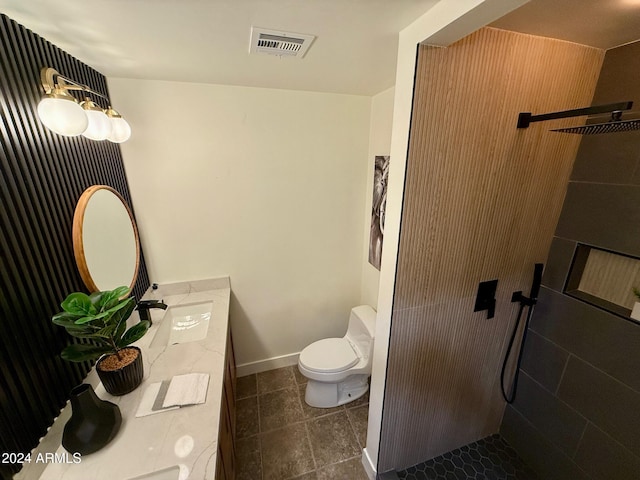 bathroom featuring tile patterned flooring, a tile shower, vanity, and toilet