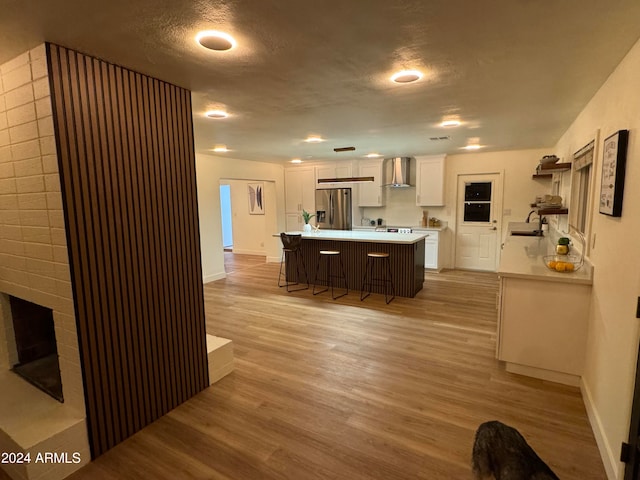 kitchen featuring sink, wall chimney range hood, a breakfast bar area, white cabinetry, and stainless steel refrigerator with ice dispenser