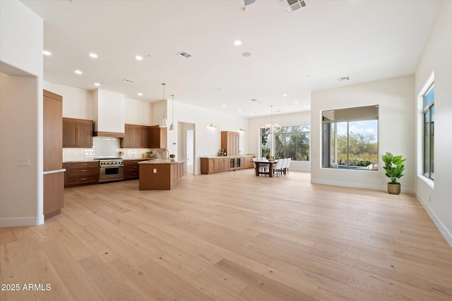 kitchen featuring a kitchen island, pendant lighting, tasteful backsplash, high end stainless steel range oven, and light hardwood / wood-style flooring