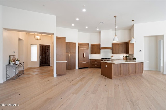 kitchen with hanging light fixtures, light wood-type flooring, paneled built in fridge, a towering ceiling, and decorative backsplash