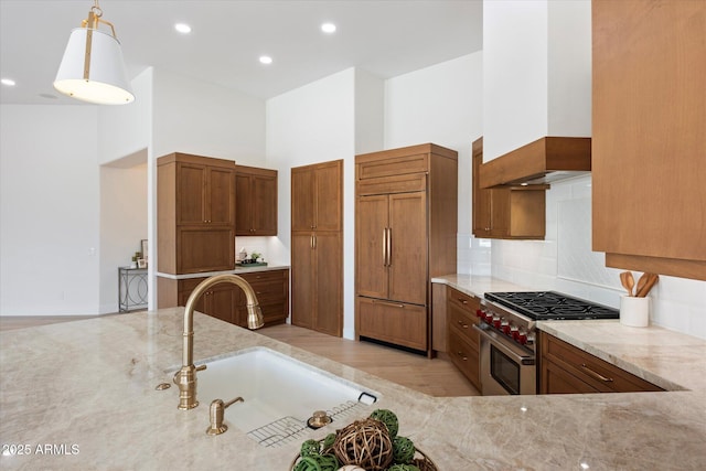 kitchen with sink, high quality appliances, light stone counters, decorative light fixtures, and custom exhaust hood