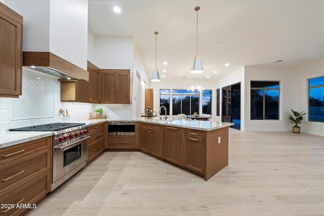 kitchen with high end range, decorative light fixtures, kitchen peninsula, custom range hood, and light stone countertops