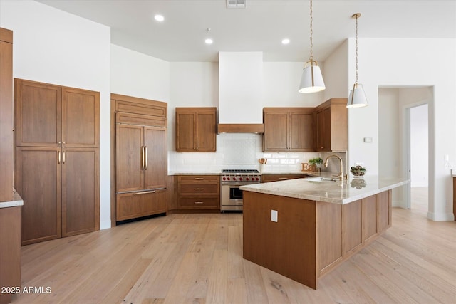 kitchen featuring sink, light wood-type flooring, high quality appliances, pendant lighting, and light stone countertops