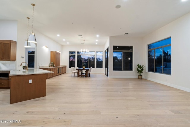 kitchen featuring sink, light stone counters, light wood-type flooring, kitchen peninsula, and pendant lighting