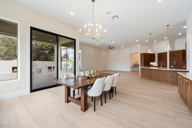 dining area with sink, ceiling fan with notable chandelier, and light wood-type flooring