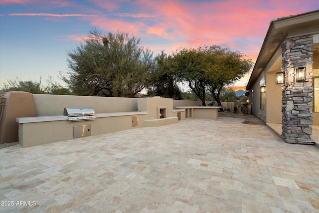 patio terrace at dusk featuring an outdoor fireplace, a grill, and area for grilling