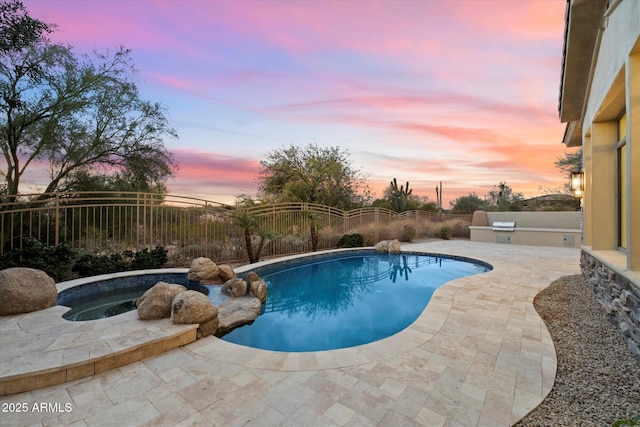 pool at dusk featuring a patio area, an in ground hot tub, and an outdoor kitchen