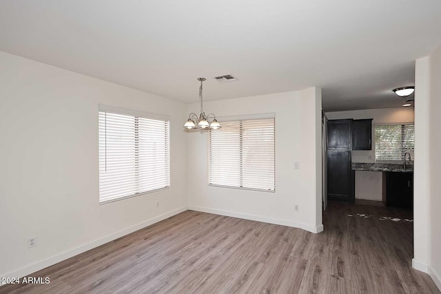 unfurnished dining area featuring a notable chandelier, a healthy amount of sunlight, sink, and dark hardwood / wood-style floors