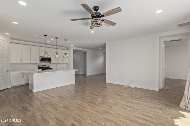 kitchen with a kitchen island with sink, white cabinets, pendant lighting, and appliances with stainless steel finishes