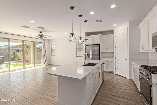 kitchen with a center island with sink, white cabinets, sink, ceiling fan, and appliances with stainless steel finishes