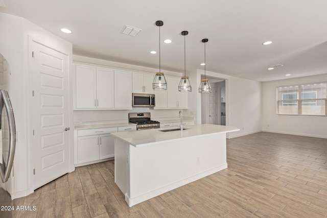 kitchen with appliances with stainless steel finishes, sink, decorative light fixtures, light hardwood / wood-style flooring, and white cabinets