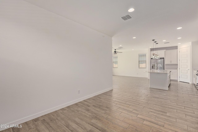 unfurnished living room featuring ceiling fan with notable chandelier and light hardwood / wood-style flooring