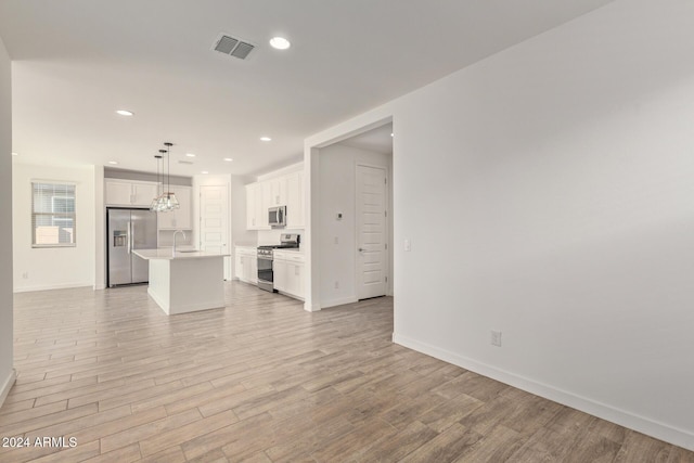 kitchen with appliances with stainless steel finishes, light wood-type flooring, pendant lighting, white cabinetry, and an island with sink