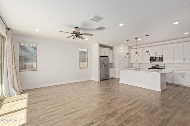 kitchen featuring white cabinetry, hanging light fixtures, light hardwood / wood-style floors, a center island with sink, and appliances with stainless steel finishes