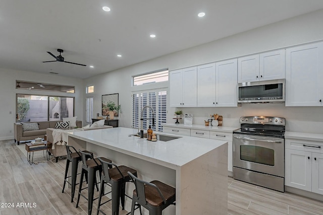 kitchen with a breakfast bar, white cabinets, a center island with sink, sink, and appliances with stainless steel finishes