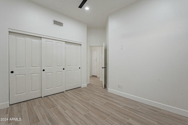 unfurnished bedroom featuring ceiling fan, a closet, a high ceiling, and light wood-type flooring