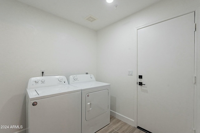 laundry area with washing machine and clothes dryer and light wood-type flooring