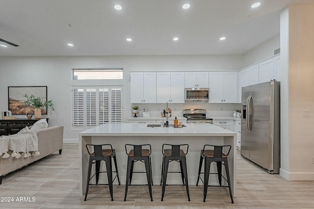 kitchen with an island with sink, a breakfast bar, white cabinets, and stainless steel appliances