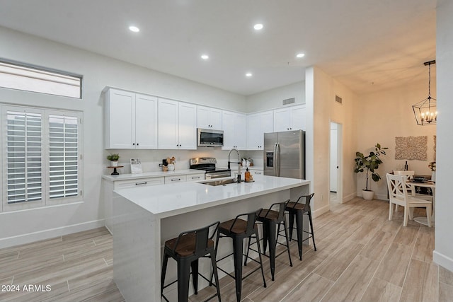 kitchen with a breakfast bar, a kitchen island with sink, sink, white cabinetry, and stainless steel appliances