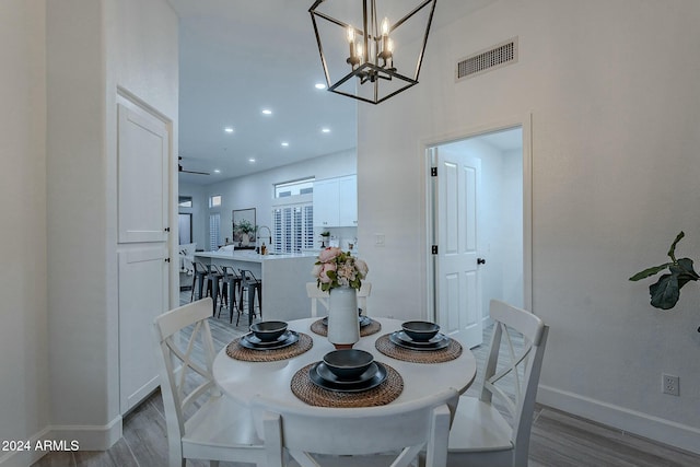 dining space with ceiling fan with notable chandelier, light hardwood / wood-style flooring, and sink