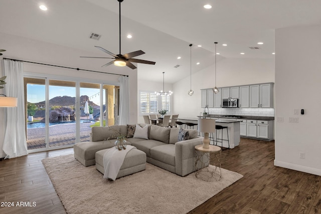 living room with ceiling fan with notable chandelier, high vaulted ceiling, a healthy amount of sunlight, and dark hardwood / wood-style flooring