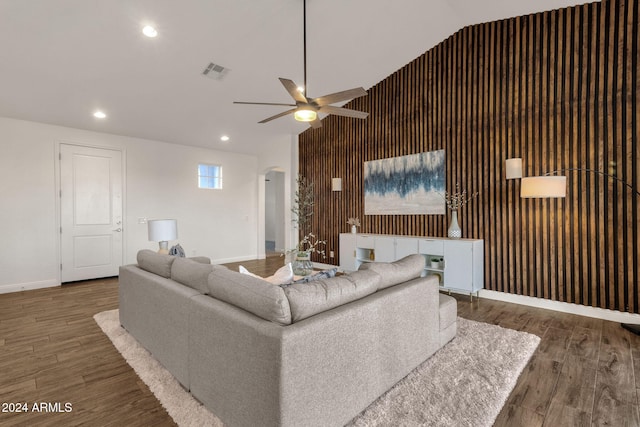 living room featuring wooden walls, dark wood-type flooring, ceiling fan, and vaulted ceiling