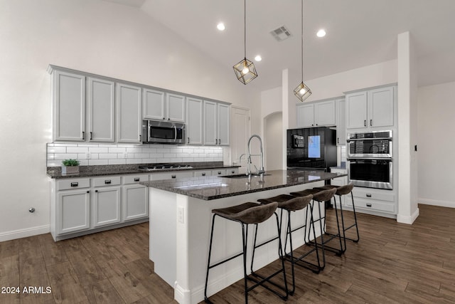 kitchen with stainless steel appliances, tasteful backsplash, high vaulted ceiling, a kitchen island with sink, and dark hardwood / wood-style flooring