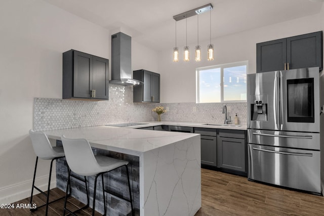 kitchen with dark wood-type flooring, light stone counters, kitchen peninsula, wall chimney exhaust hood, and stainless steel fridge with ice dispenser