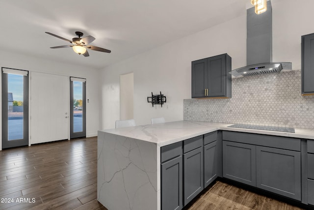 kitchen with black electric cooktop, gray cabinets, wall chimney range hood, and kitchen peninsula