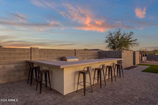 patio terrace at dusk with an outdoor bar and area for grilling