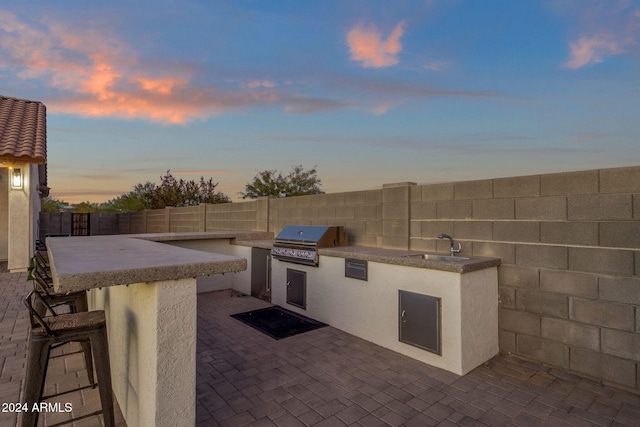 patio terrace at dusk featuring exterior kitchen and area for grilling