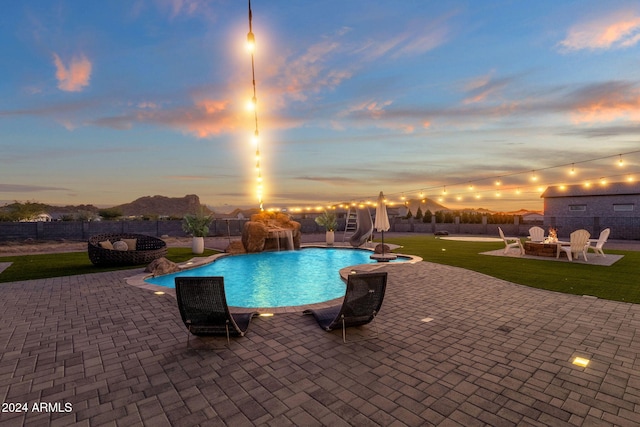 pool at dusk with a patio, a fire pit, a water slide, and a yard