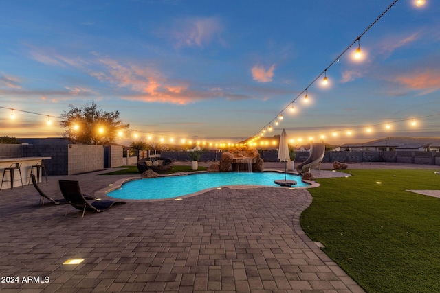 pool at dusk featuring a patio area, a yard, and a water slide