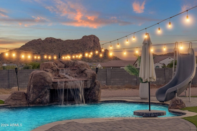 pool at dusk with a water slide and pool water feature