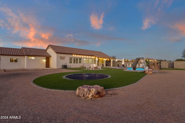 back house at dusk featuring central AC unit, a patio area, and a yard