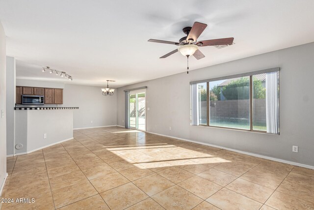 tiled spare room featuring ceiling fan with notable chandelier