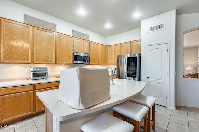 kitchen with light tile patterned flooring, appliances with stainless steel finishes, a breakfast bar area, and a center island with sink