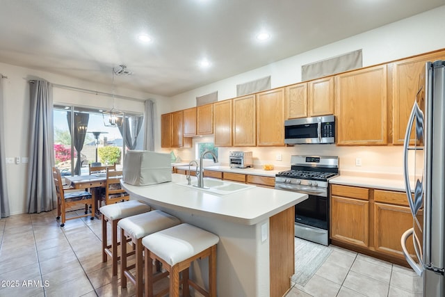 kitchen featuring sink, a breakfast bar area, a kitchen island with sink, stainless steel appliances, and decorative light fixtures