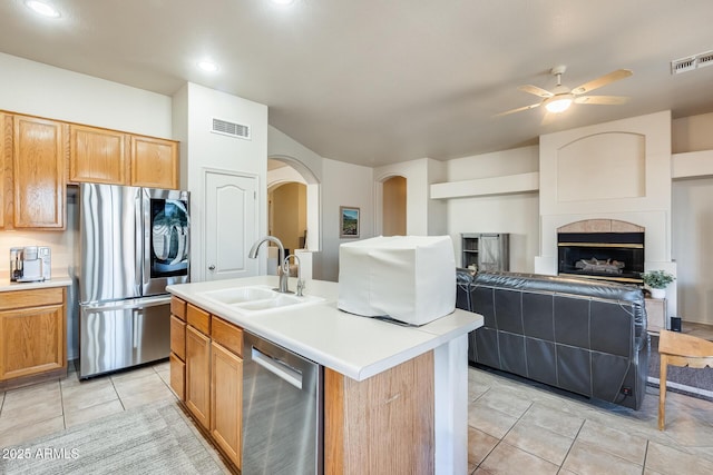 kitchen featuring sink, light tile patterned floors, a tile fireplace, a kitchen island with sink, and stainless steel appliances