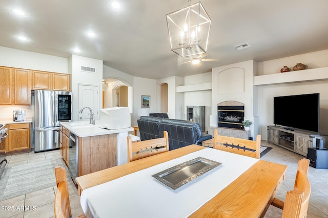 kitchen with light tile patterned floors, sink, appliances with stainless steel finishes, an island with sink, and decorative light fixtures