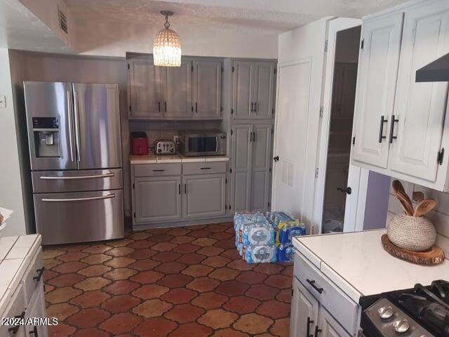 5539 N 31st Ln, Phoenix, AZ 85017 - kitchen with appliances with stainless steel finishes, tile countertops, gray cabinetry, wall chimney exhaust hood, and hanging light fixtures