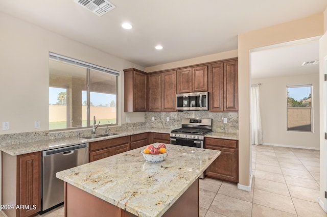 kitchen featuring sink, tasteful backsplash, appliances with stainless steel finishes, a kitchen island, and light stone countertops