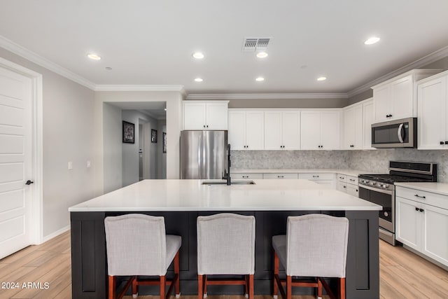 kitchen with a center island with sink, backsplash, light hardwood / wood-style floors, crown molding, and stainless steel appliances