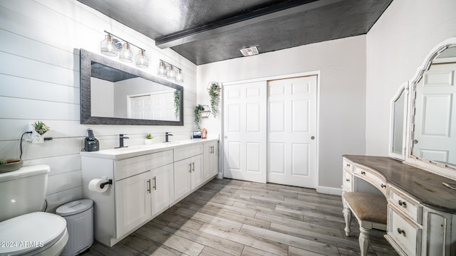 bathroom featuring beamed ceiling, vanity, hardwood / wood-style flooring, and toilet