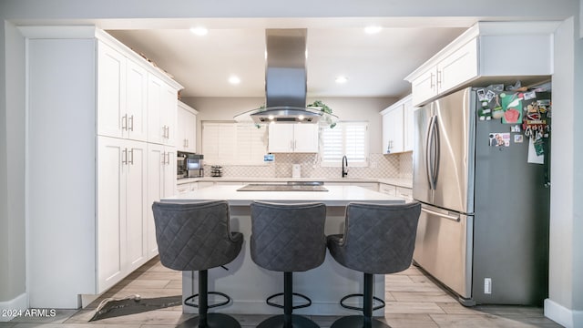 kitchen with stainless steel refrigerator, white cabinets, island range hood, a kitchen island, and light wood-type flooring