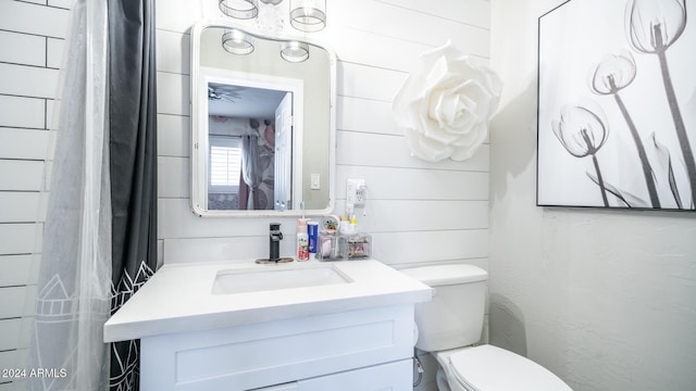 bathroom featuring ceiling fan, wood walls, toilet, and vanity