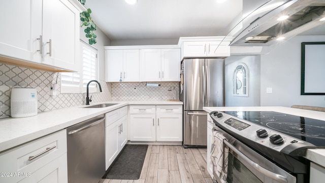 kitchen with appliances with stainless steel finishes, wall chimney exhaust hood, sink, light hardwood / wood-style flooring, and white cabinets