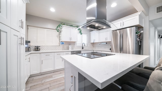 kitchen with island range hood, stainless steel appliances, light hardwood / wood-style floors, white cabinetry, and a breakfast bar area