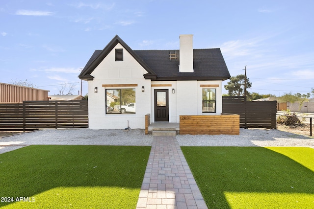 view of front of house with a shingled roof, a chimney, fence, and a front yard