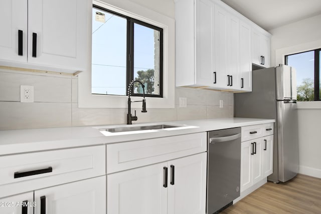 kitchen featuring a sink, white cabinetry, light wood-type flooring, dishwasher, and tasteful backsplash